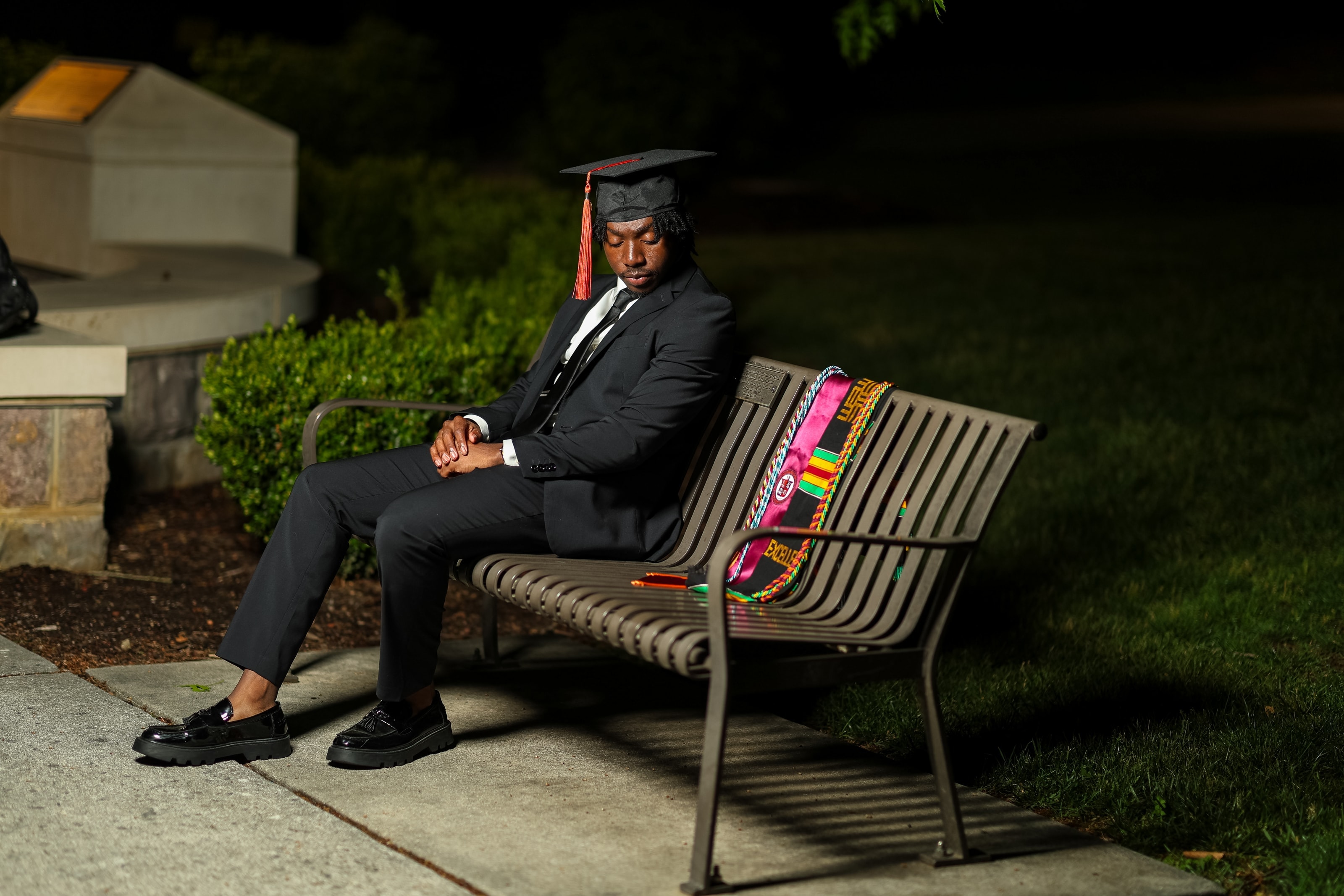 Ethan sitting on a park bench at night, eyes closed, his graduation cords laid out beside him