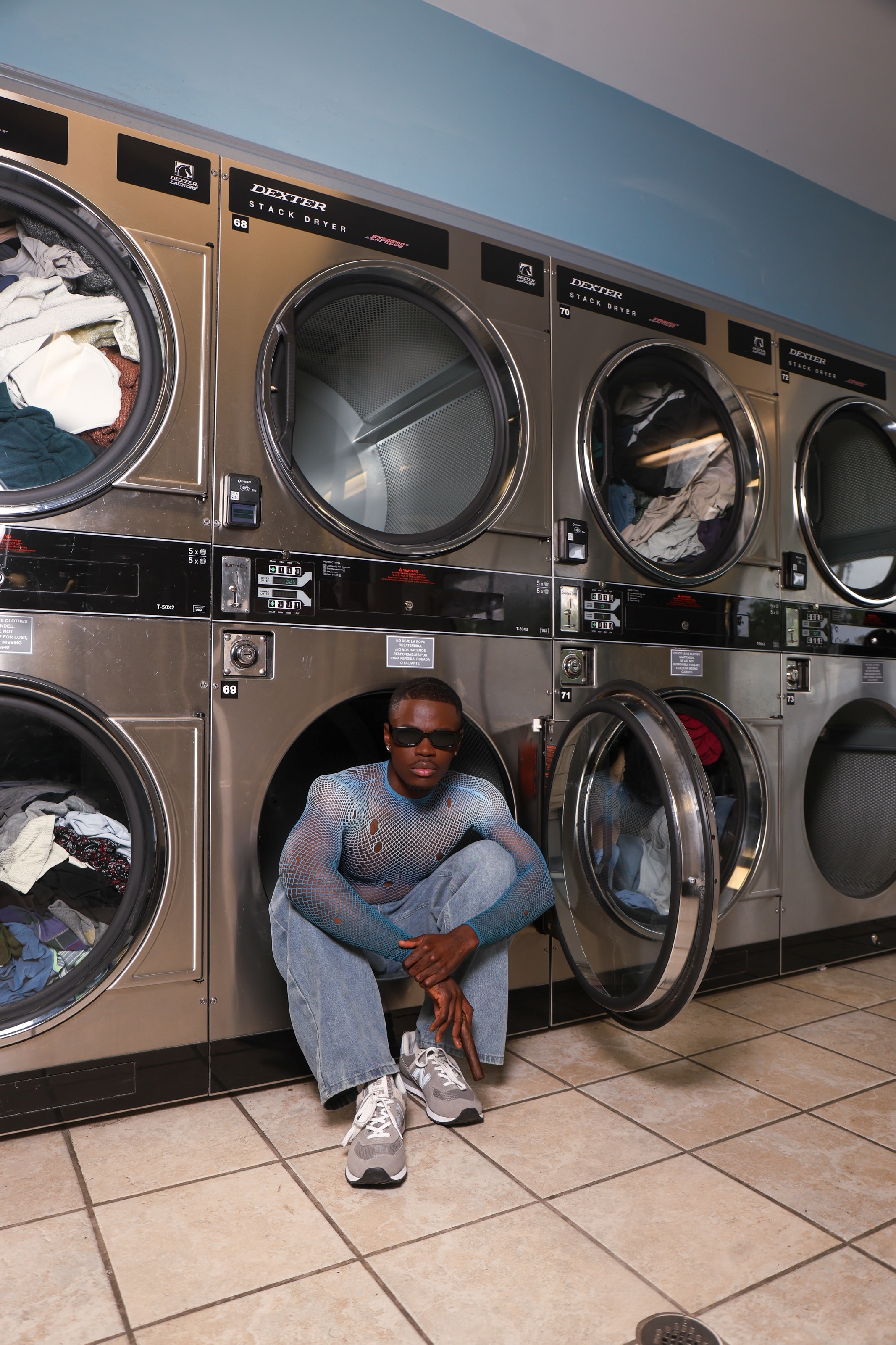 Kofi sitting inside a dryer drum, arms wrapped around his knees, looking directly into the lens