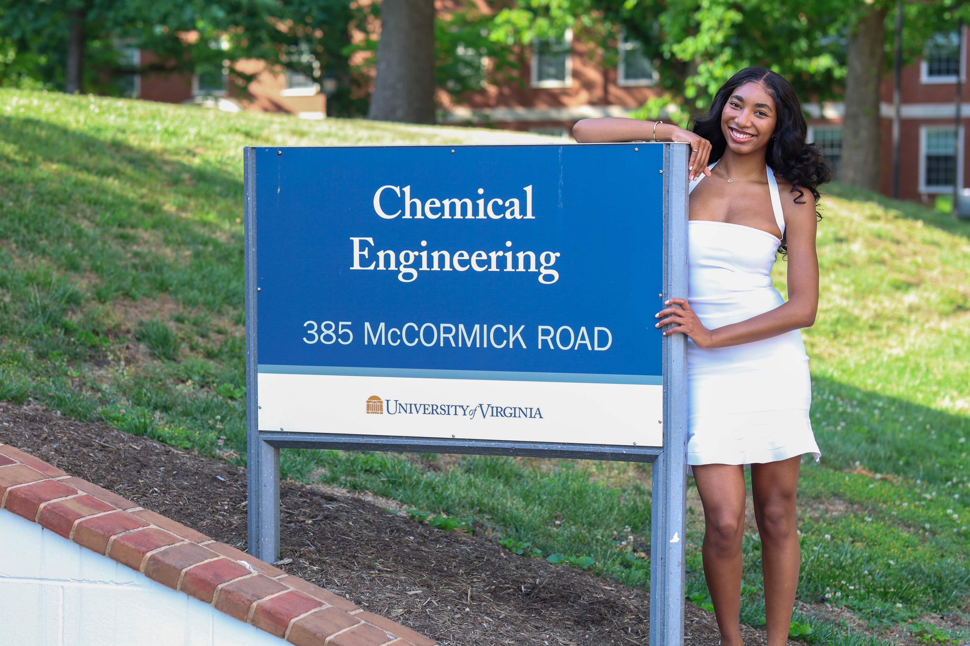Nella smiling beside a Chemical Engineering department sign on campus, one arm resting on top of it