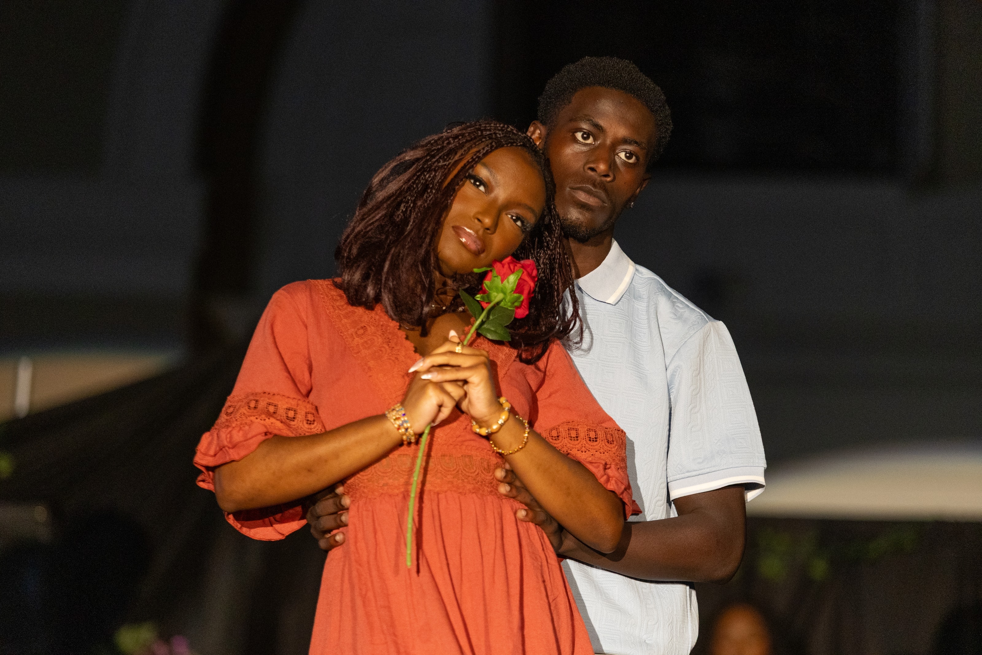 A couple posing together at night, one holding a red rose, both looking directly into the lens