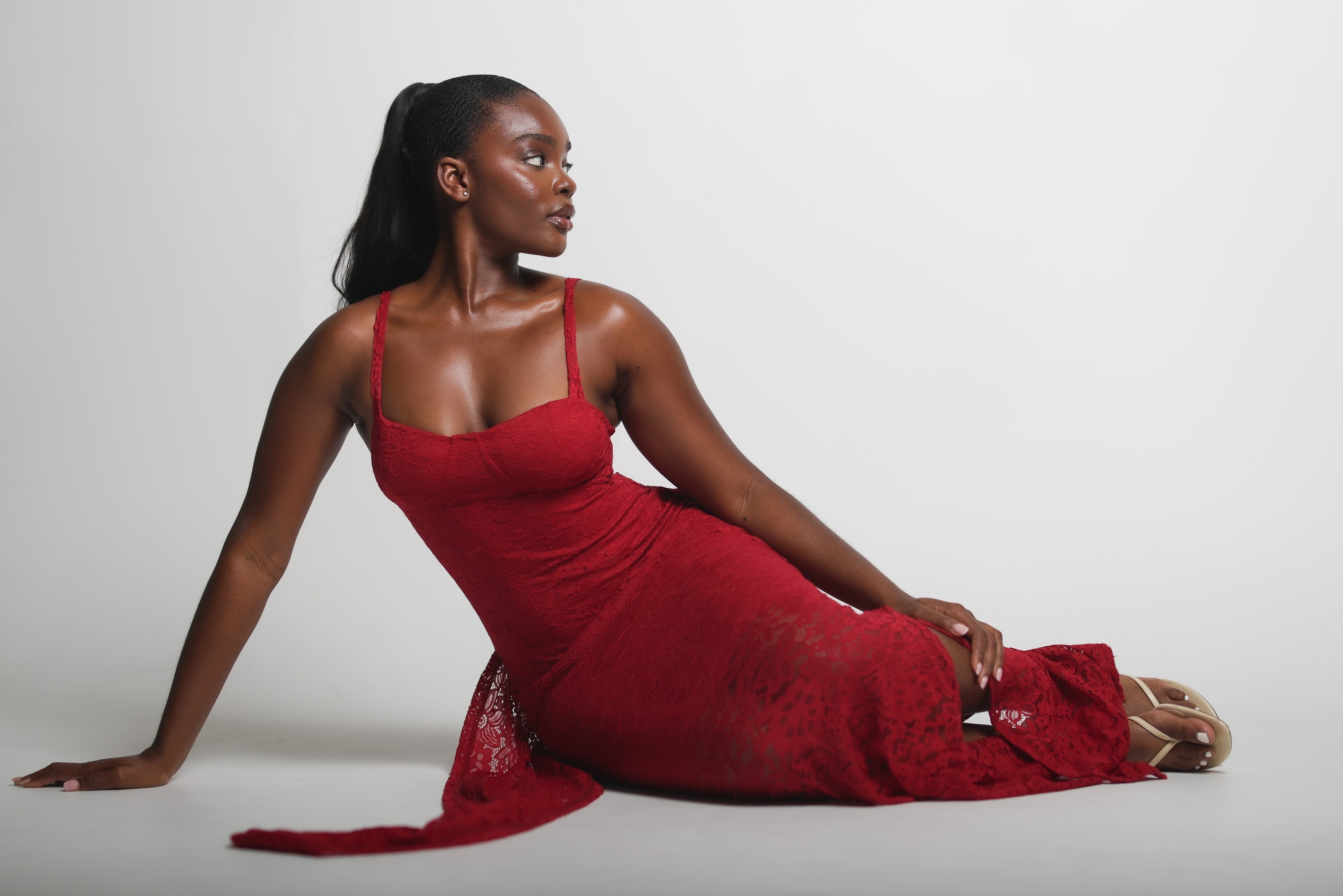Bisola reclining on the studio floor in a red lace dress, one hand on her hip, looking off to the side